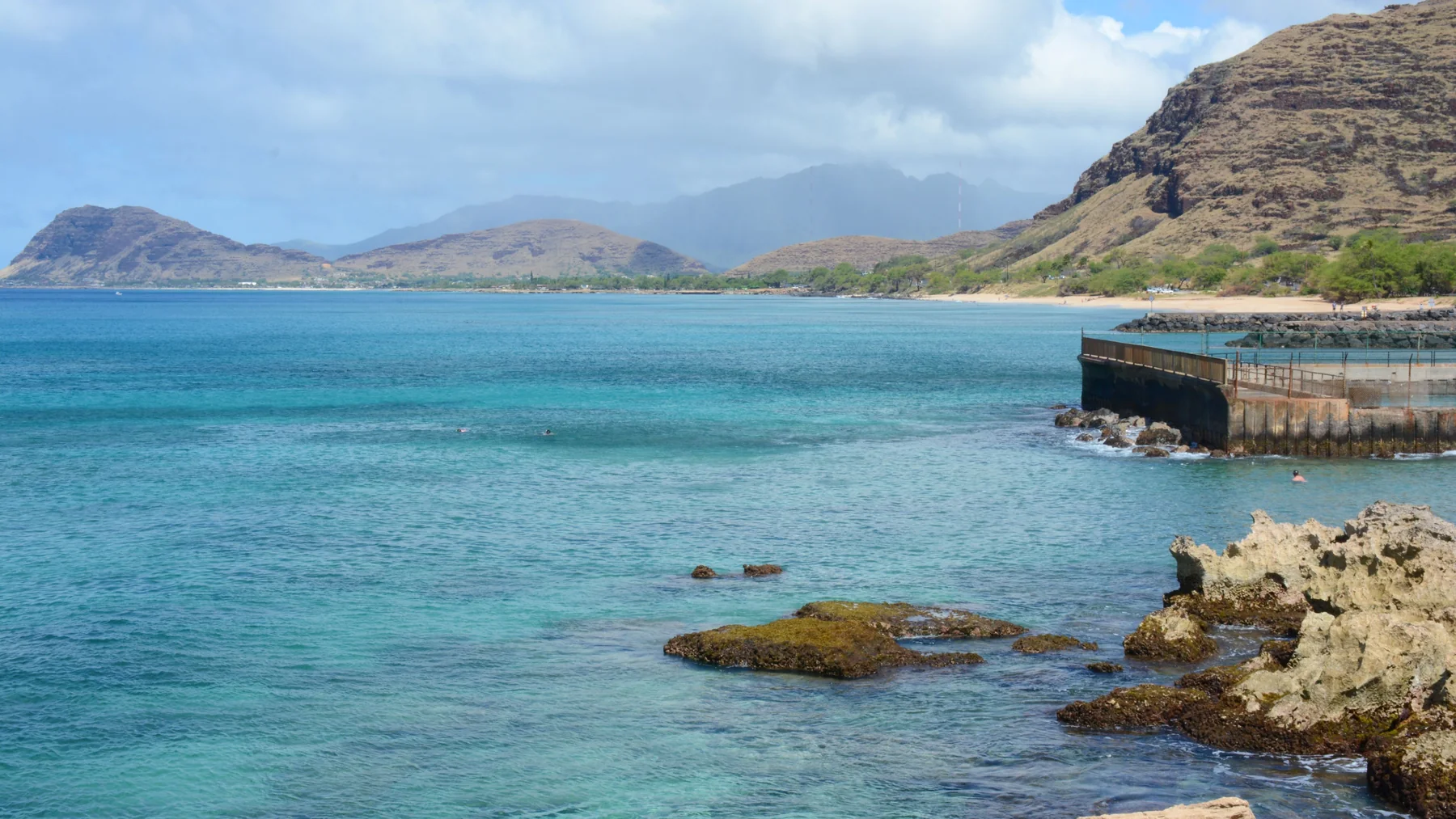 A turquoise bay and volcanic headland along Oʻahu's leeward coast near Kapolei, swimmers in the calm water